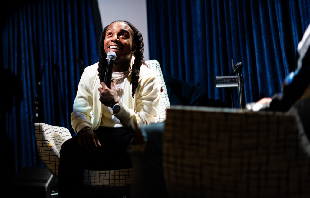 Singer holds mic while sitting down at an event
